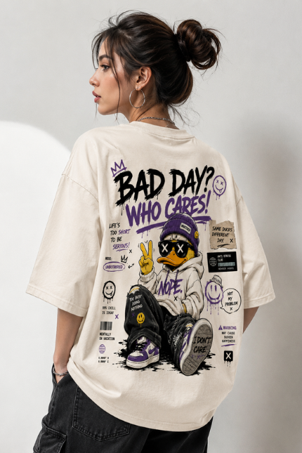 Woman wearing Luri Bad Day Who Cares graphic oversized t-shirt — cream unisex streetwear tee with graffiti duck character, "Bad Day? Who Cares!" grunge text, smiley faces and purple sticker graphics, back view