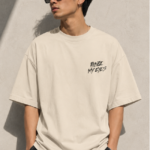 Man wearing Luri Before My Eyes anime graphic oversized t-shirt — cream tee back view showing dark anime illustration of spinning eye motifs with crow feathers and "Any Technique Is Worthless Before My Eyes" grunge text