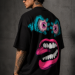 Man wearing Luri Chaos Face graphic oversized t-shirt — black unisex surrealist art tee with bulging teal eyeballs and giant hot-pink open mouth graphic, back view