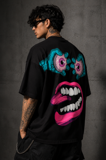 Man wearing Luri Chaos Face graphic oversized t-shirt — black unisex surrealist art tee with bulging teal eyeballs and giant hot-pink open mouth graphic, back view