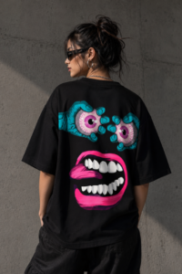 Woman wearing Luri Chaos Face graphic oversized t-shirt — black unisex art tee with surrealist monster face print in teal and hot pink, back view, oversized fit