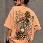 Woman wearing Luri Monkey King graphic oversized t-shirt in peach — unisex tee with anime-ukiyo-e Sun Wukong illustration wielding golden staff, pink clouds and Japanese kanji, back view