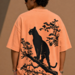 Man wearing Luri Silent Panther graphic oversized t-shirt in terracotta — back view showing black panther silhouette perched on a tree branch with floral details on premium Supima Cotton