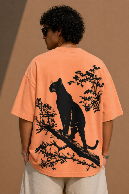 Man wearing Luri Silent Panther graphic oversized t-shirt in terracotta — back view showing black panther silhouette perched on a tree branch with floral details on premium Supima Cotton