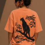 Woman wearing Luri Silent Panther graphic oversized t-shirt in terracotta — back view with black panther on tree branch botanical silhouette print, unisex oversized fit