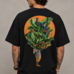 Man wearing Luri Tropical Soul graphic oversized t-shirt — black unisex tee with richly illustrated tropical figure, banana leaves and macaw parrots in an orange sun circle, back view